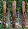 Three tall wooden tiki totem statues with carved geometric patterns outdoors in a garden.