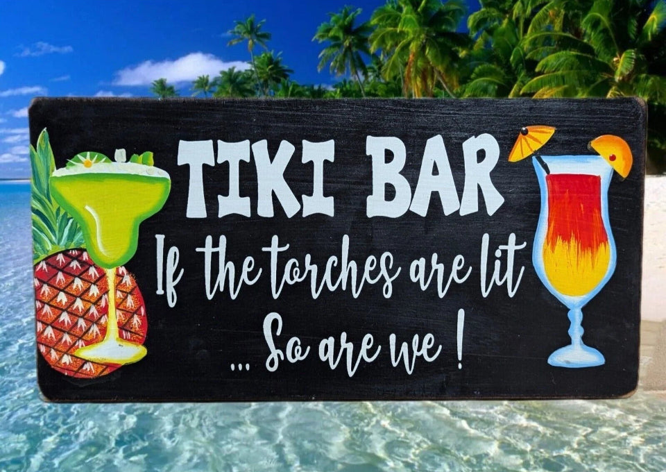 Tiki bar chalkboard sign on a tropical beach with pineapple drink and colorful cocktail.