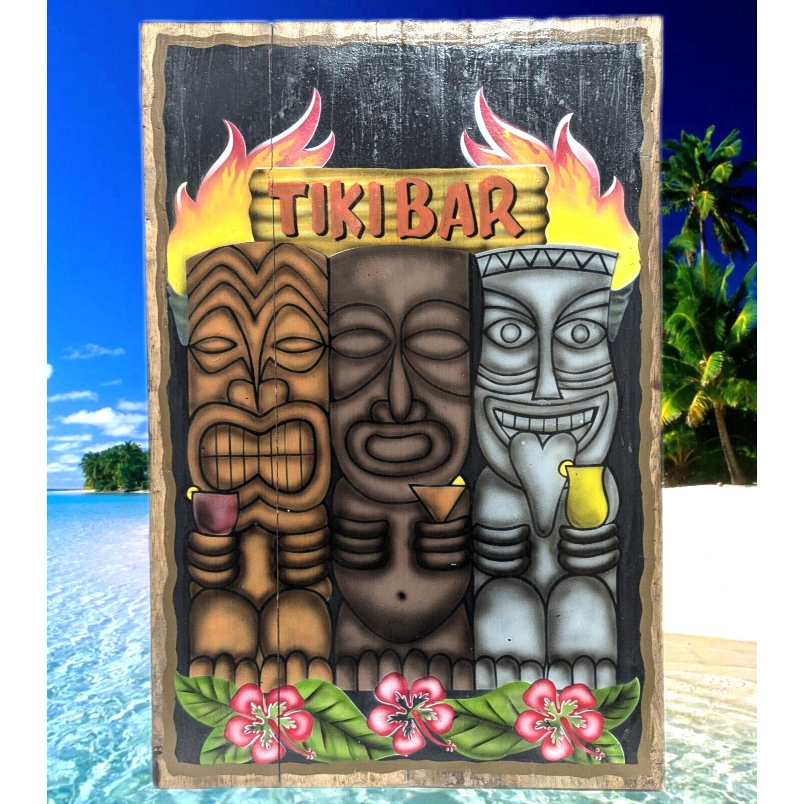 Three tiki faces on a flaming tiki bar sign at the beach with hibiscus flowers