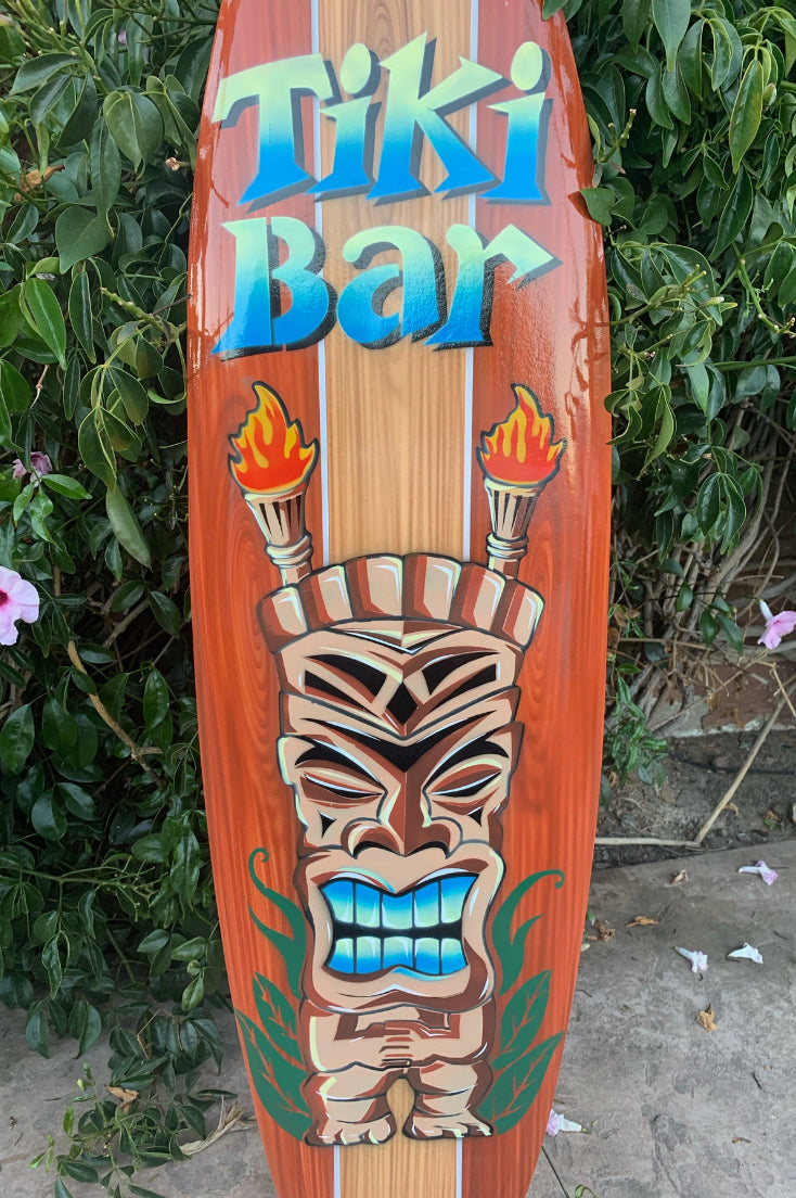 Decorative tiki bar wooden surfboard with carved tiki mask and torches