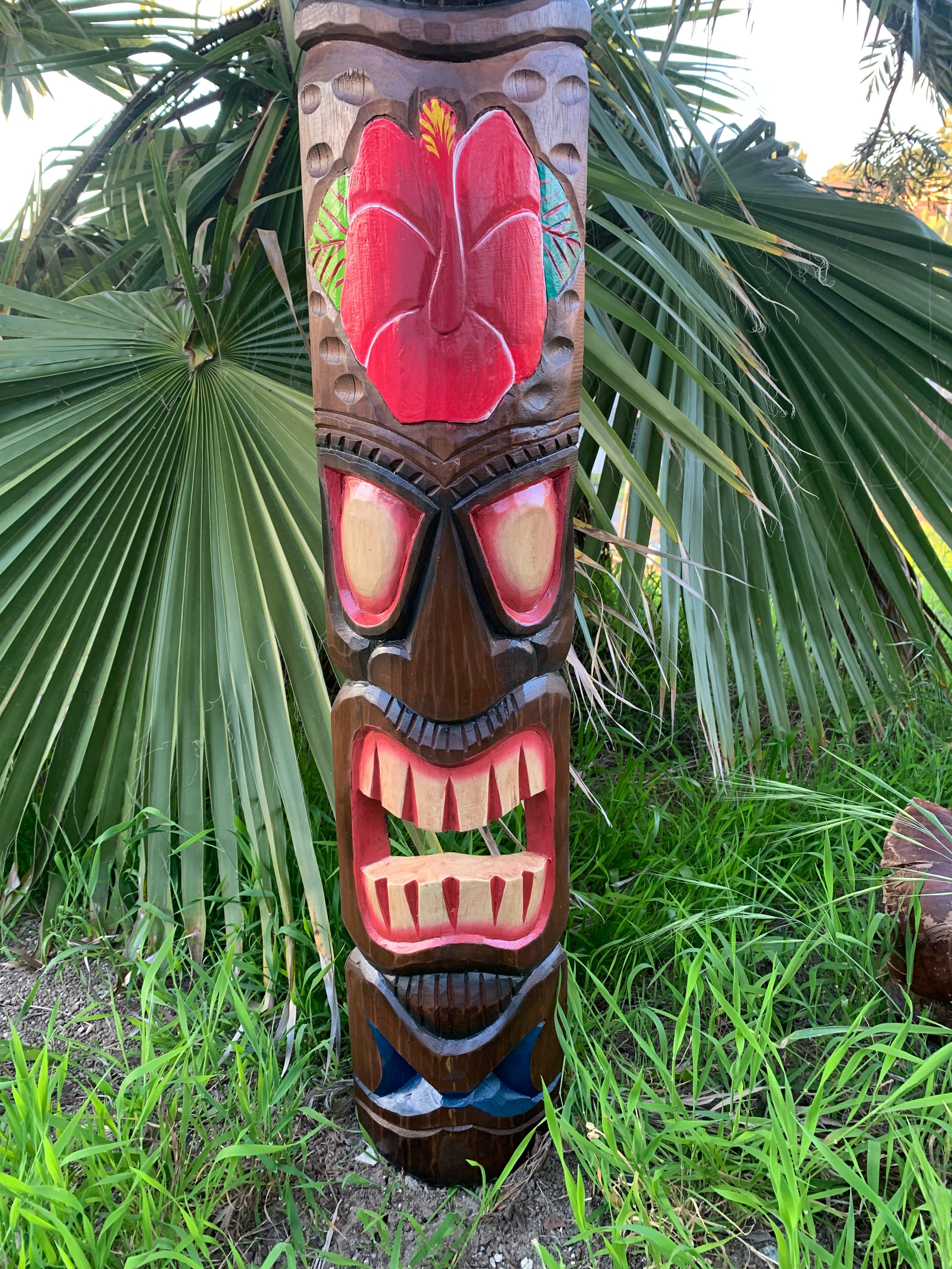Carved wooden tiki pole with a red face in a tropical garden