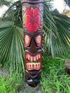 Carved wooden tiki pole with a red face in a tropical garden