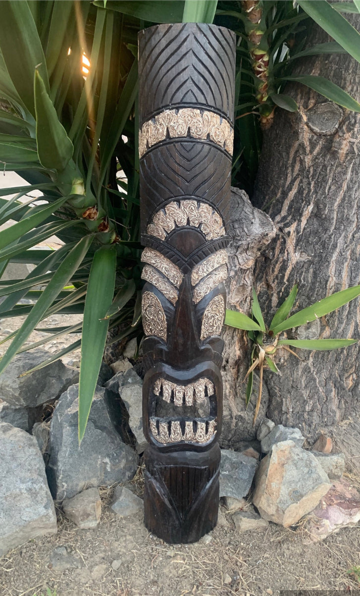Black carved tiki totem statue with beige detailing in a garden setting