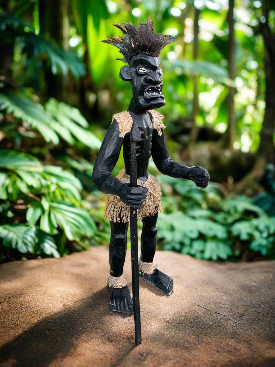 Black wooden tiki statue with burlap loincloth in a lush garden
