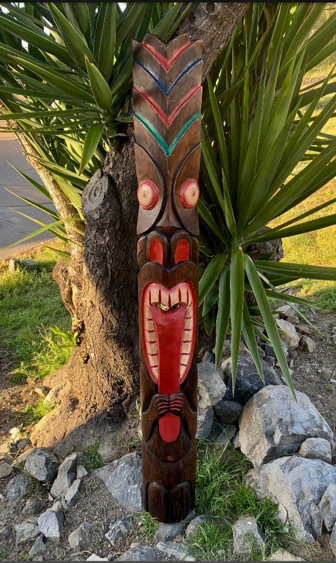 Carved wooden tiki totem with a red face and green accents in a garden.