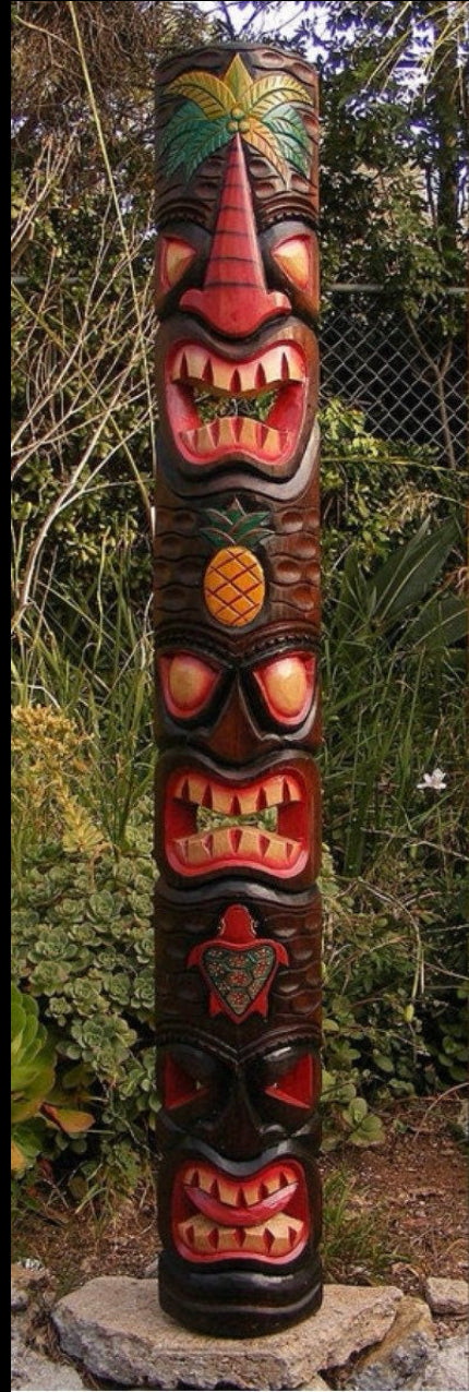 Carved tiki totem pole with multiple faces and a pineapple motif in a garden.