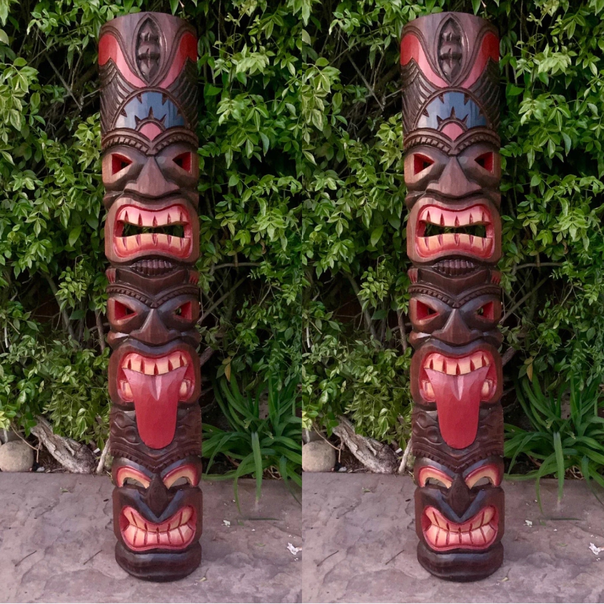 Two carved tiki totem poles with stacked faces in a garden