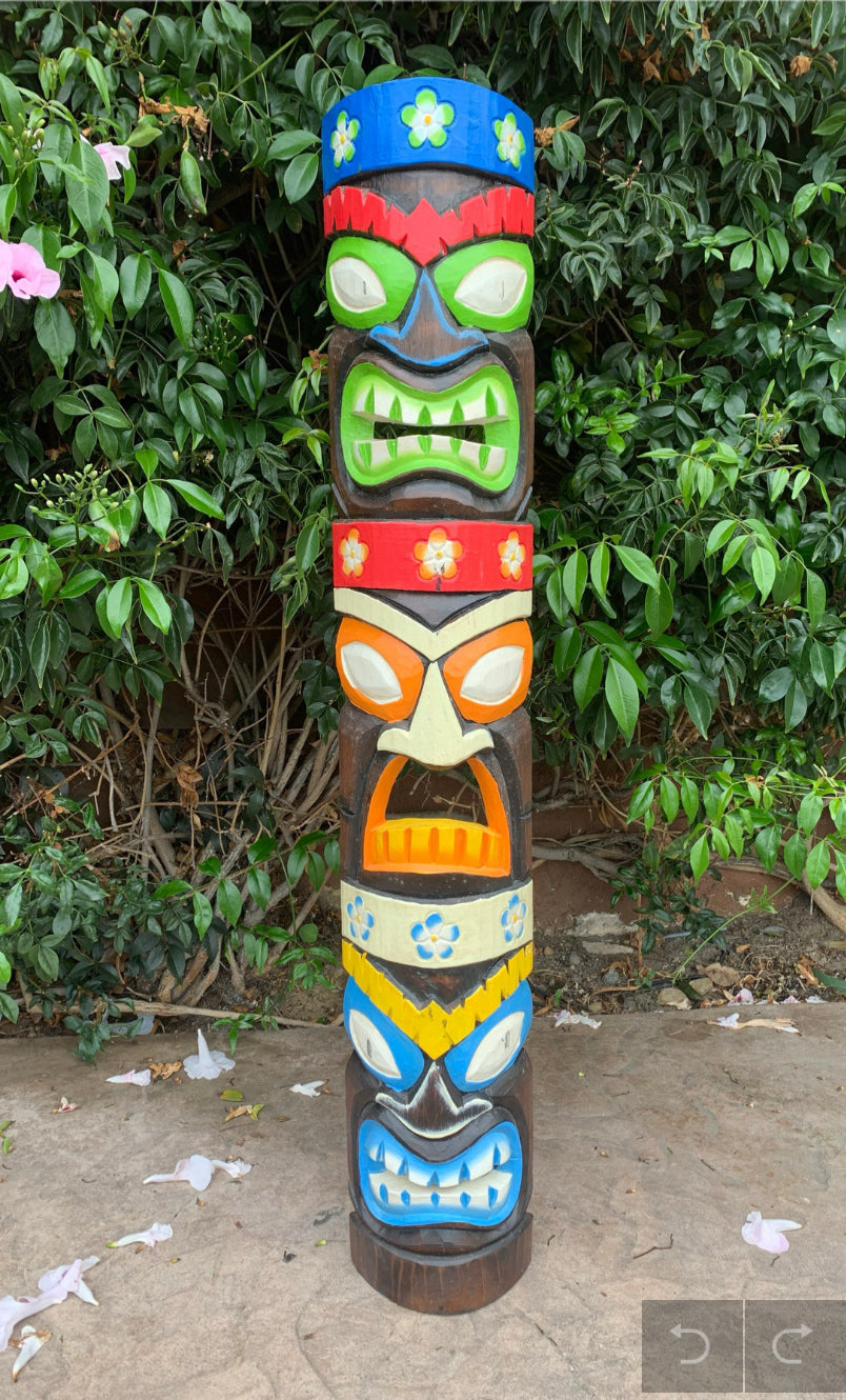Colorful multi-face tiki totem pole carved from wood in a garden setting