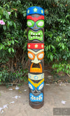 Colorful multi-face tiki totem pole carved from wood in a garden setting