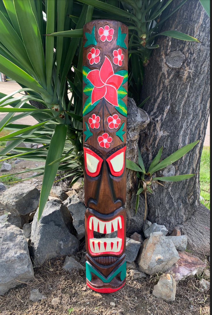 carved tiki totem pole featuring red flower designs, red eyes, and a toothy mouth outdoors