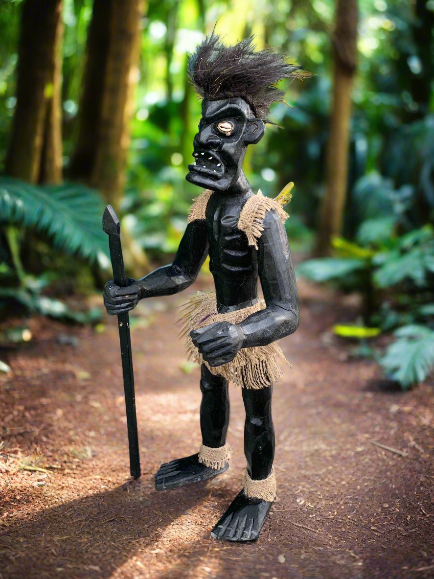 black tiki statue holding a spear in a forest path