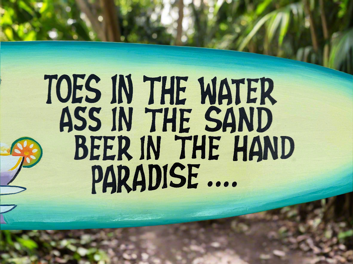 Surfboard with tropical quote that reads toes in the water ass in the sand beer in the hand paradise