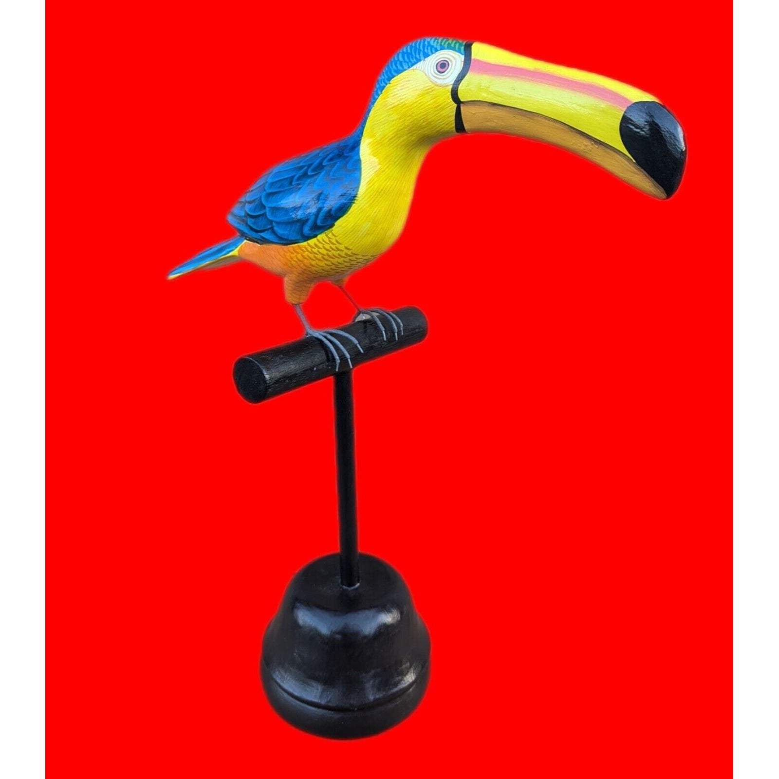 Colorful toucan figurine perched on a stand against a bright red background.