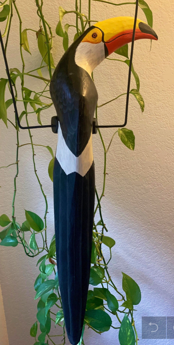 Wooden toucan sculpture with yellow beak and black body among hanging green plants