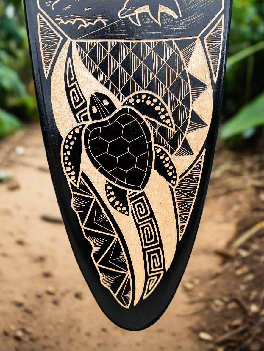 Intricately carved tan sea turtle and geometric patterns on a black surface