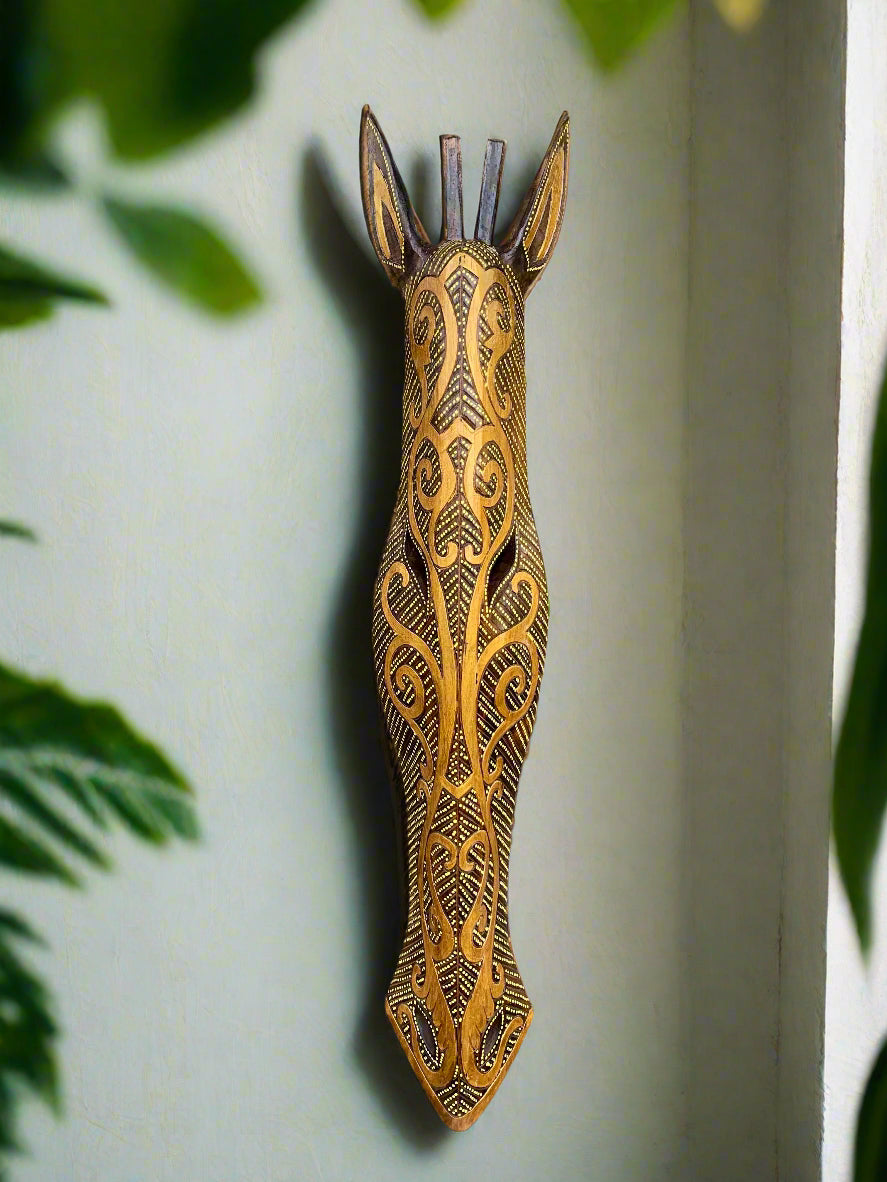 Tribal-patterned wooden giraffe sculpture leaning against a tree outdoors