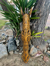 Tribal-patterned wooden giraffe sculpture leaning against a tree outdoors