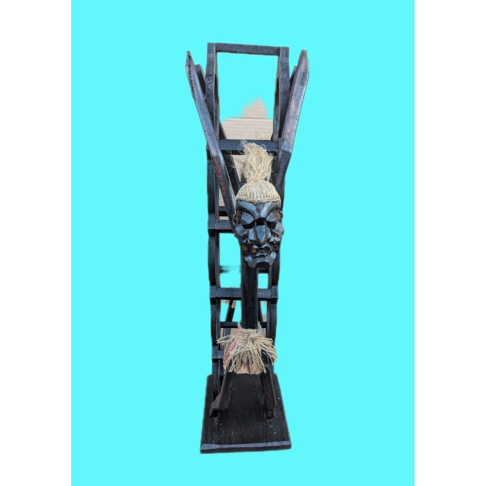 Dark wooden tiki statue with rope hair against turquoise background