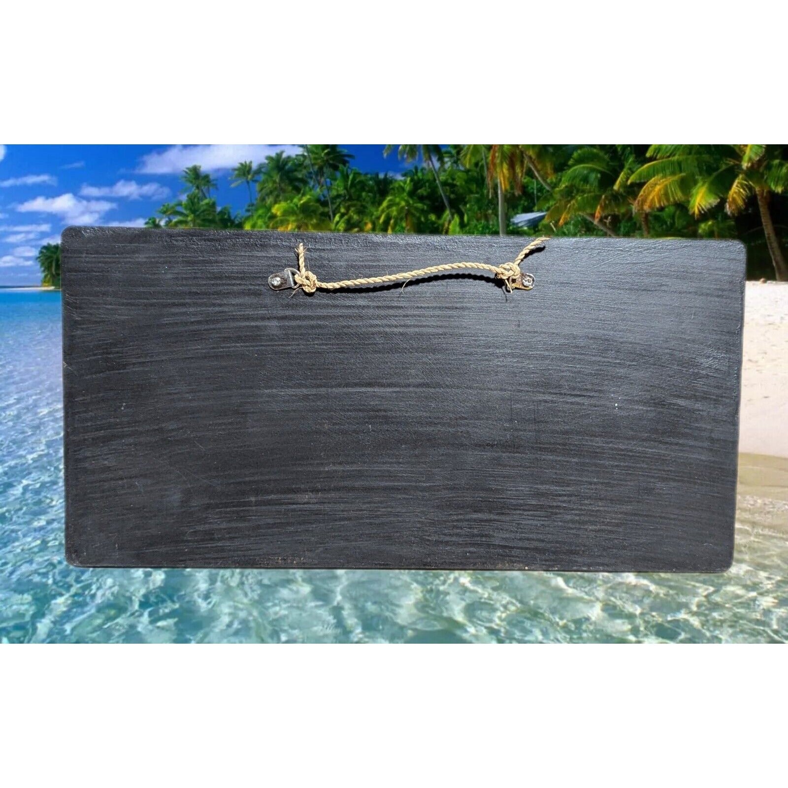 Black wooden signboard with rope hanger on a tropical beach