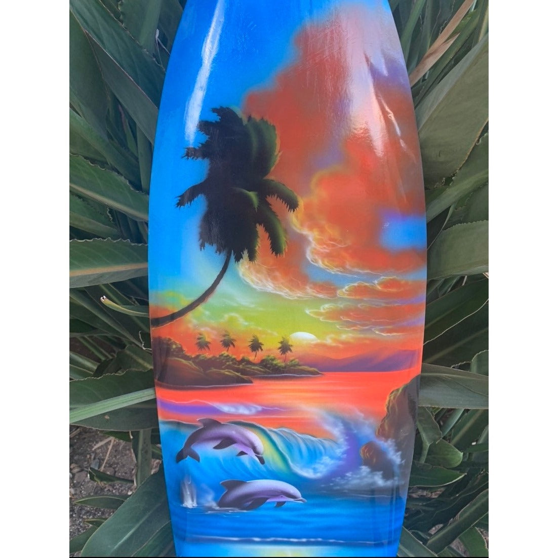 Colorful tropical sunset on a surfboard with palm trees and dolphins.