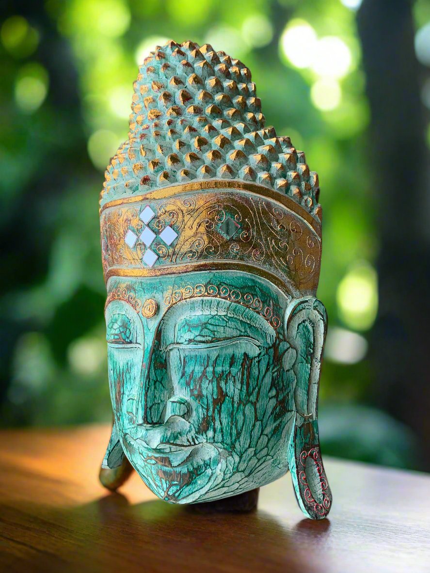 Turquoise Buddha head statue with an ornate crown and intricate patterns in a garden setting.