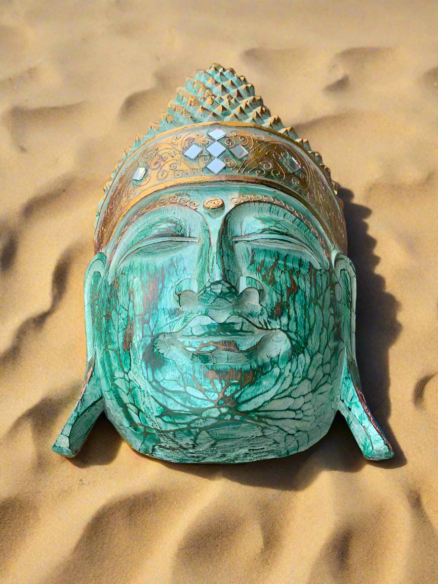 turquoise Buddha head statue with ornate headdress partially buried in sand