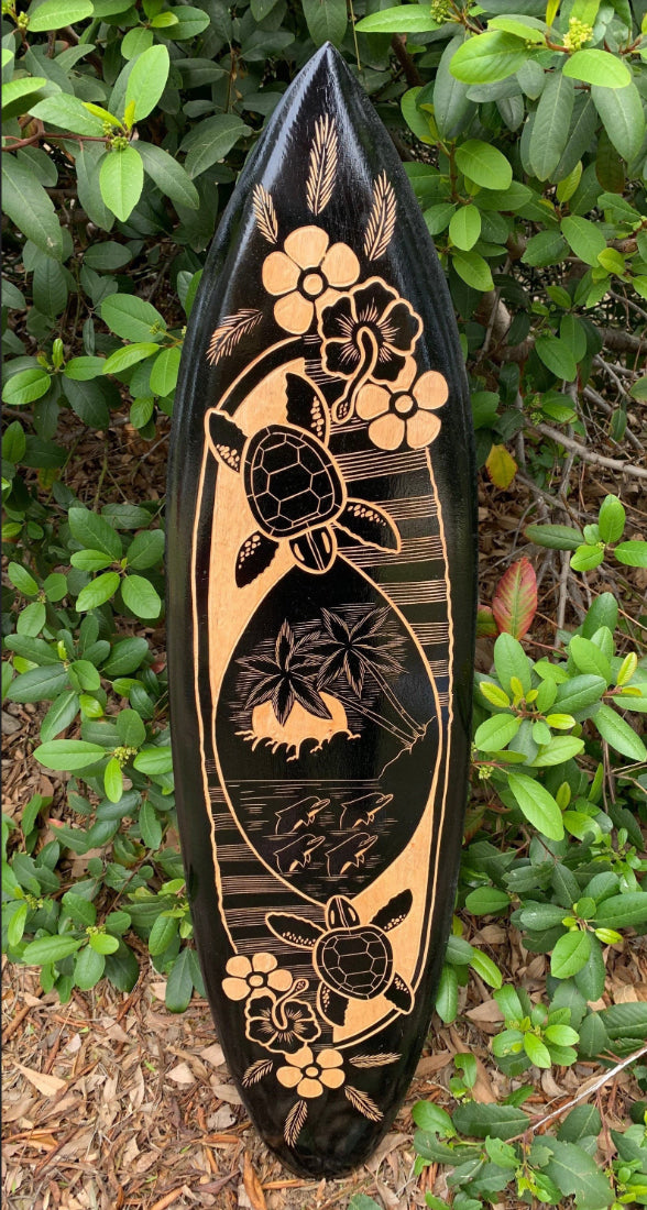 Decorative black surfboard with tan wood inlay showing a turtle, tropical flowers, palm trees and island scene