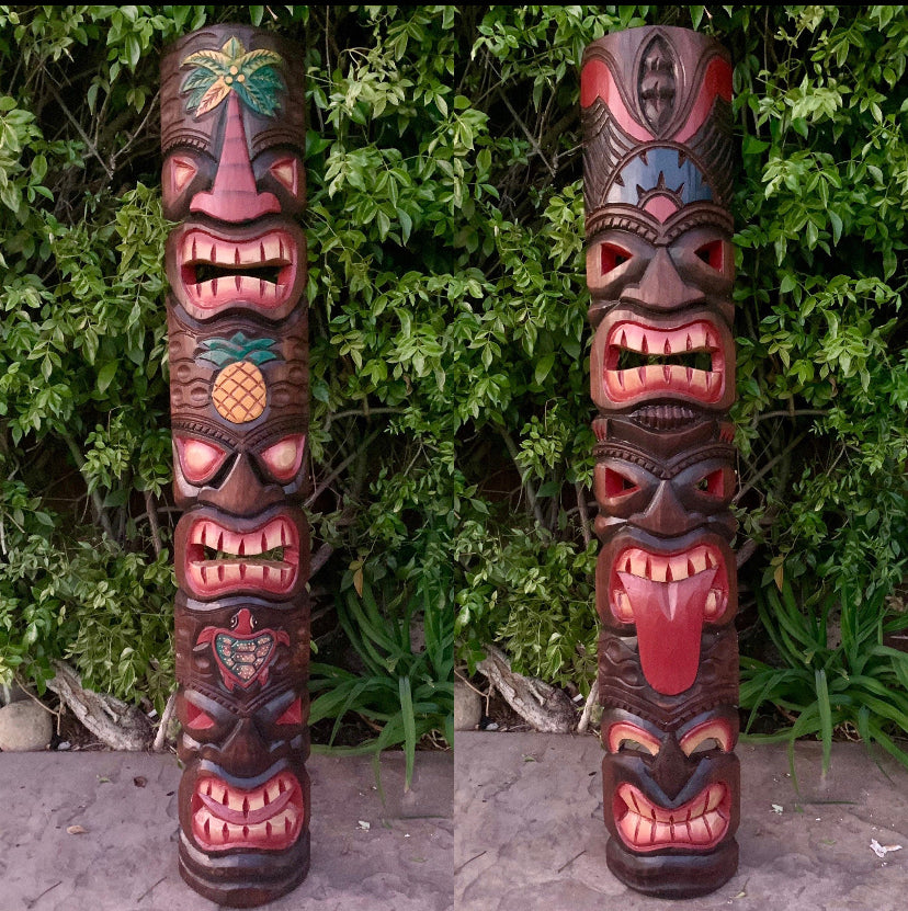 Two wooden tiki totem poles with carved faces among green foliage