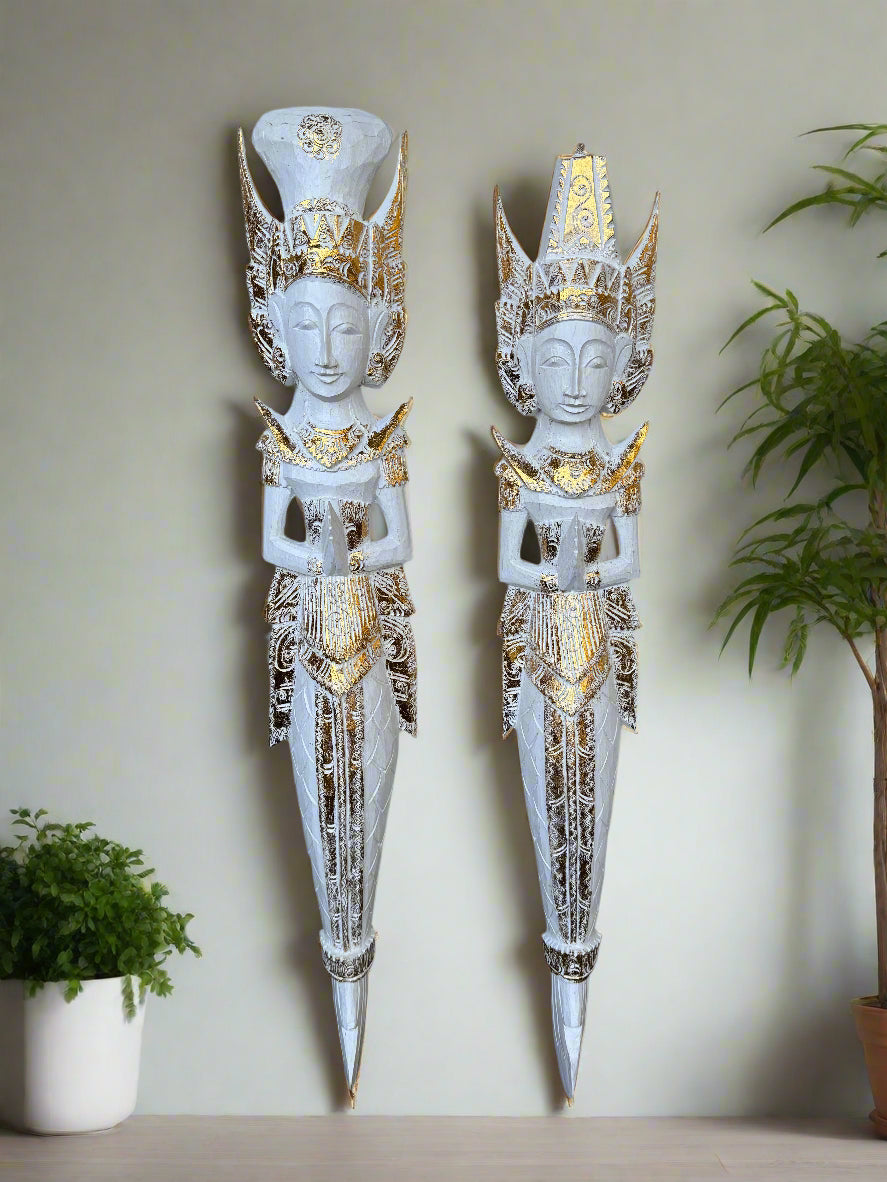 Two white and gold ornate statues with tall crowns mounted on a wall.