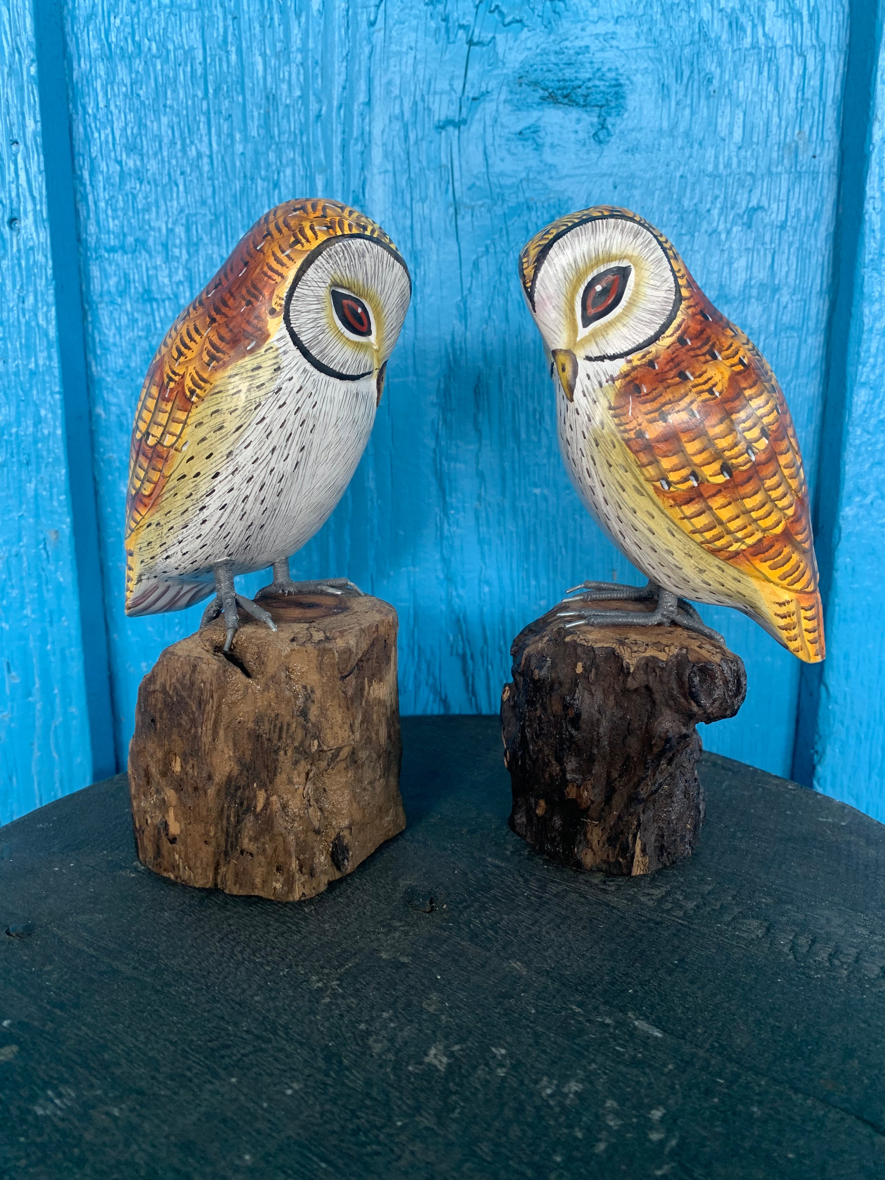 Two carved wooden owls perched on bark-stump bases against a blue background.
