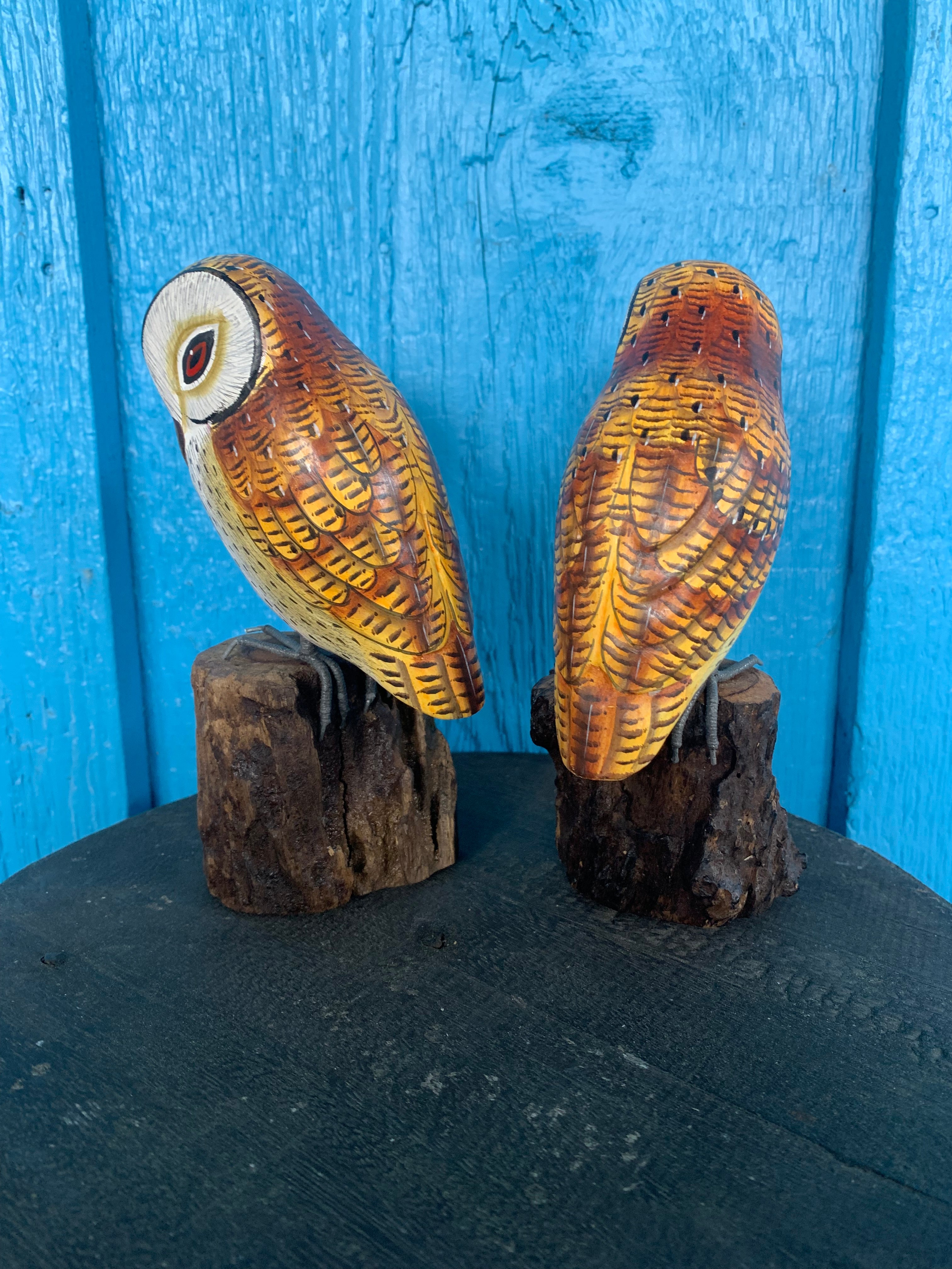 Two carved wooden owls perched on log bases against a vivid blue wooden background