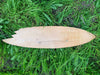 unfinished wooden surfboard blank lying on green grass