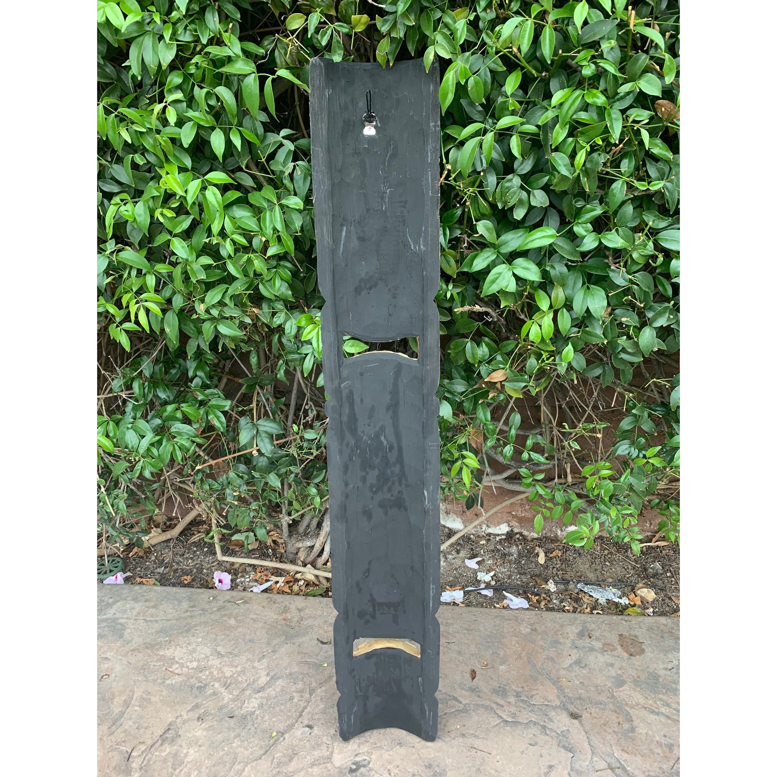 Vertical dark slate post with two rectangular cutouts outdoors near a leafy hedge
