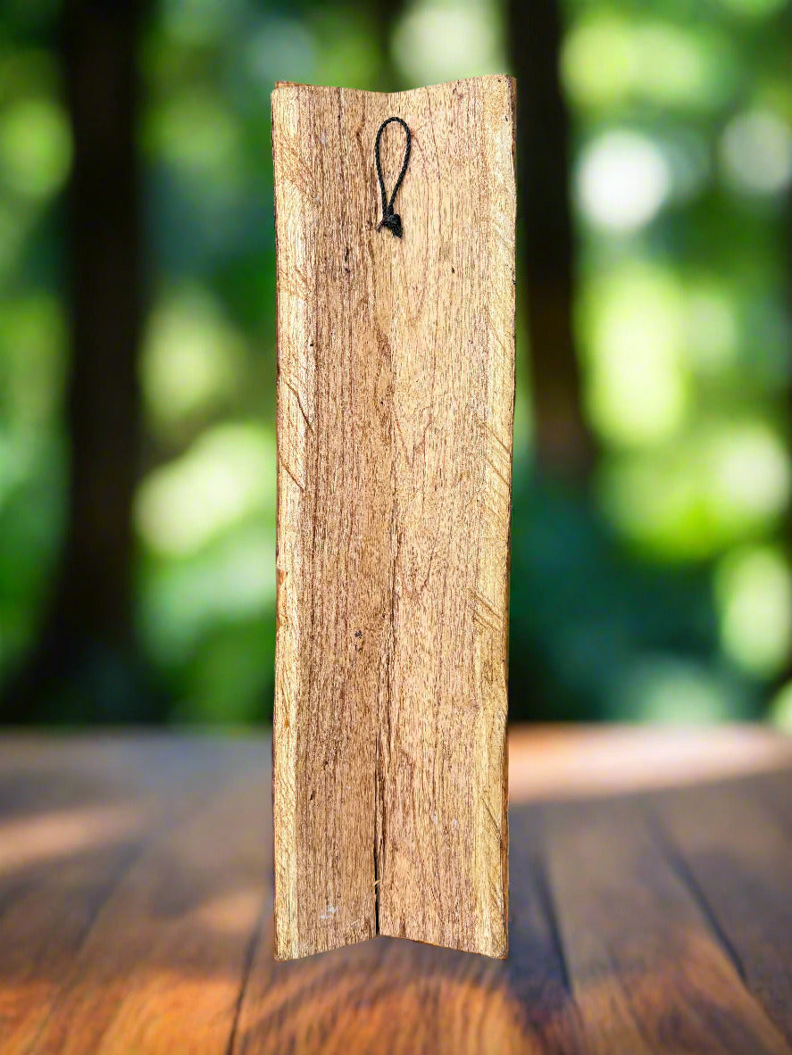 Vertical wooden plank with a hanging loop on a table in a blurred outdoor background.