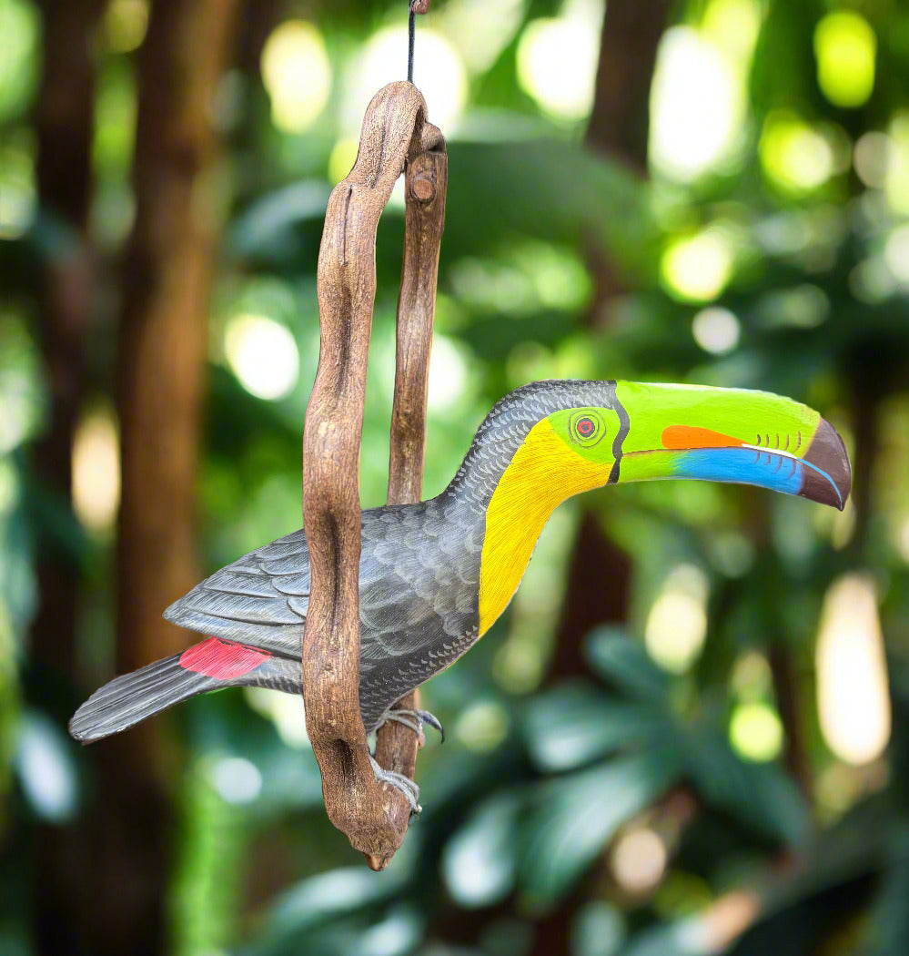 Vibrant painted toucan wood carving perched on a branch in a tropical garden.
