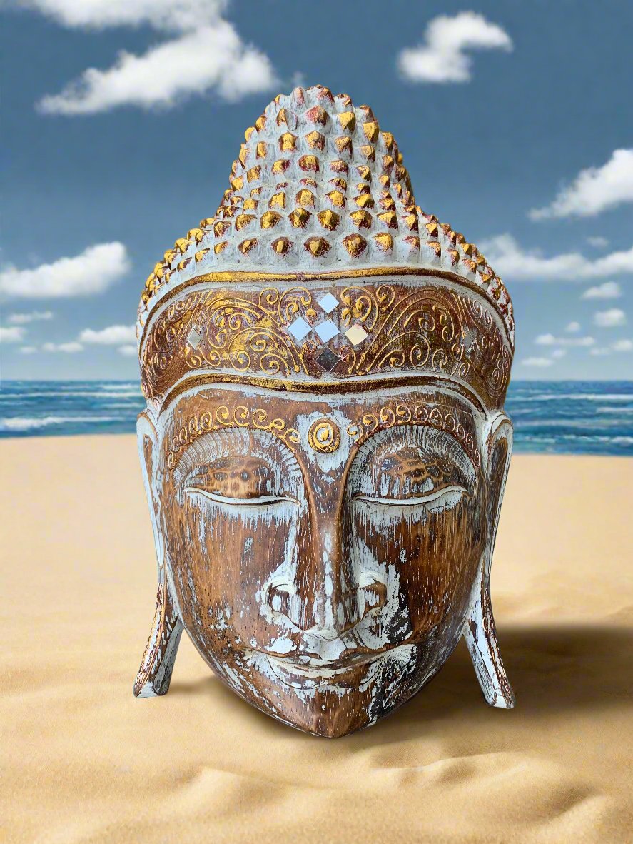 Weathered Buddha head statue on a sandy beach with the ocean in the background