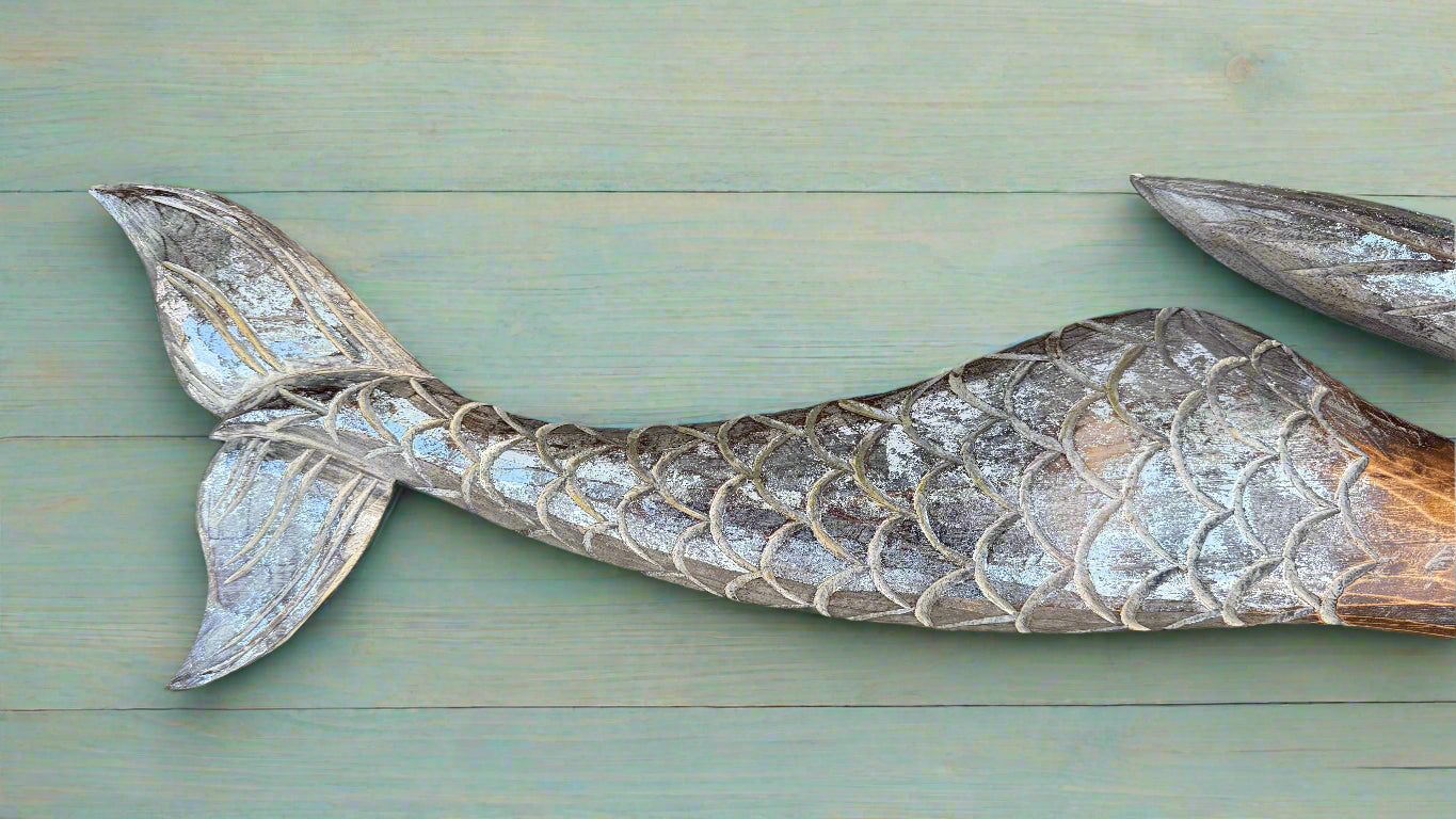 Weathered mermaid tail sculpture with fish-scale pattern on green wooden planks.