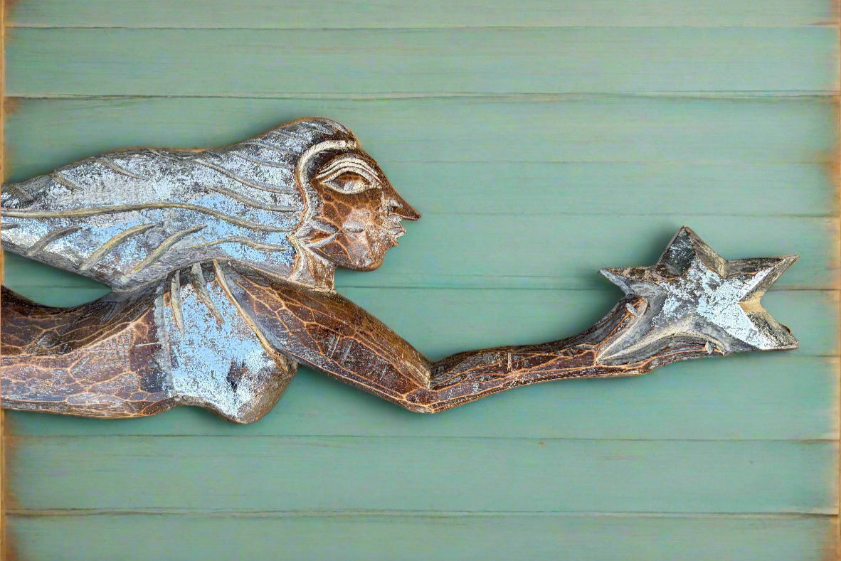 Weathered wooden angel sculpture reaching for a star against a green wooden background.
