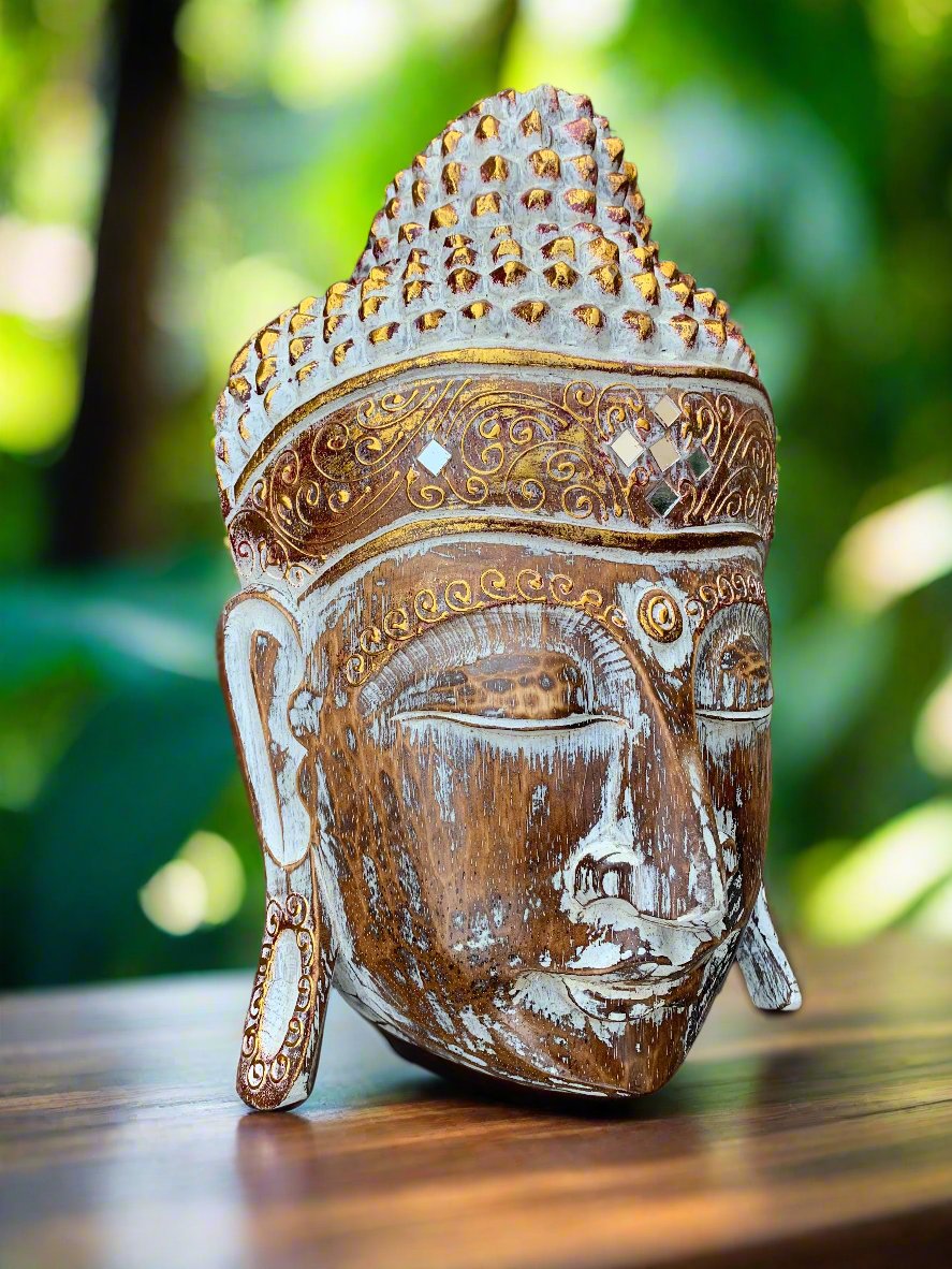 Weathered wooden Buddha head with ornate crown, outdoors in a garden