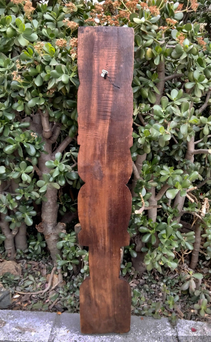 Weathered wooden carved baluster post leaning against green shrubbery