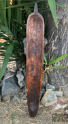 Weathered wooden paddle leaning against a tree among rocks and greenery.