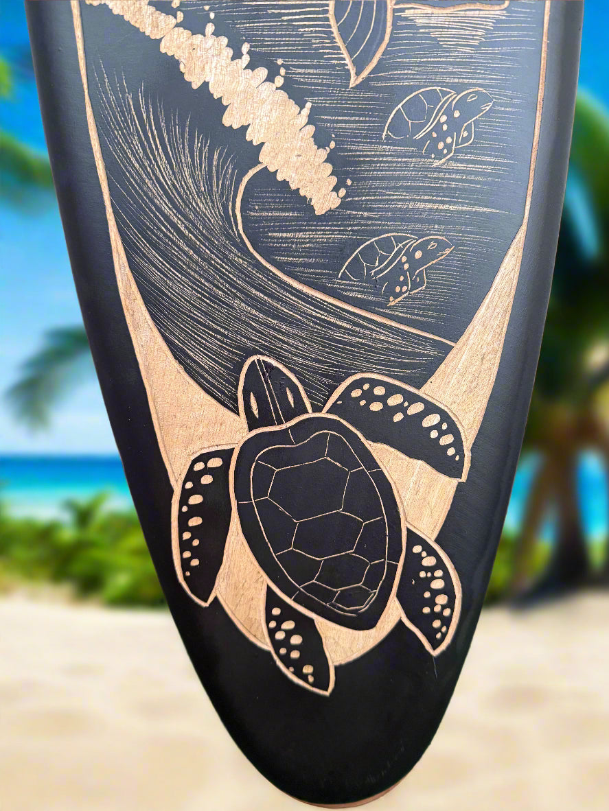 close-up of black surfboard with a wood-burn turtle and wave pattern