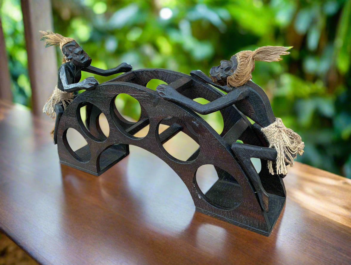 Two rope-haired wooden figurines balance on a curved arch puzzle with circular cutouts