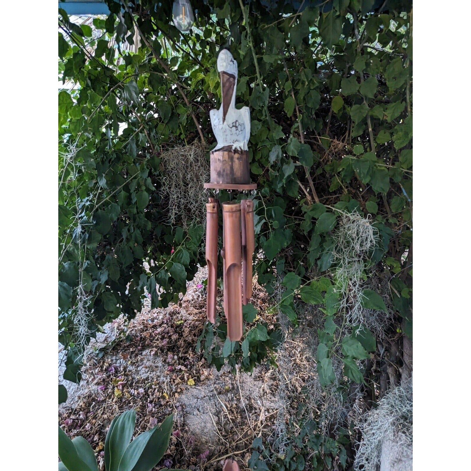 wooden bamboo wind chime hanging from a leafy garden tree