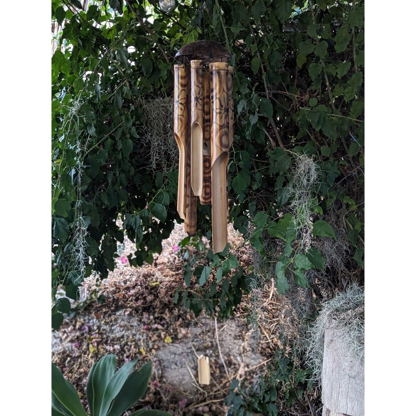 Wooden bamboo wind chimes hanging from a green leafy shrub in a garden