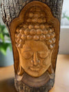 carved wooden Buddha head with closed eyes on a tree trunk, serene expression