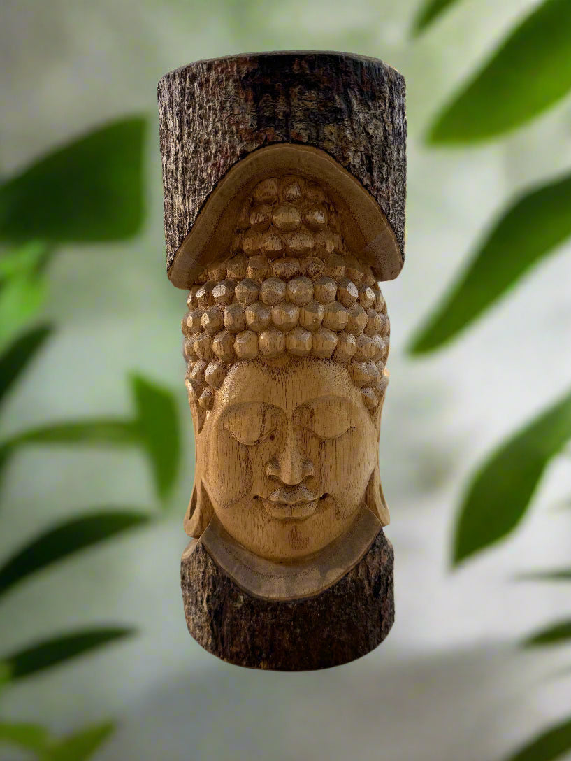 Wooden Buddha head carved on a tree stump with textured curls and a serene expression, leaf background