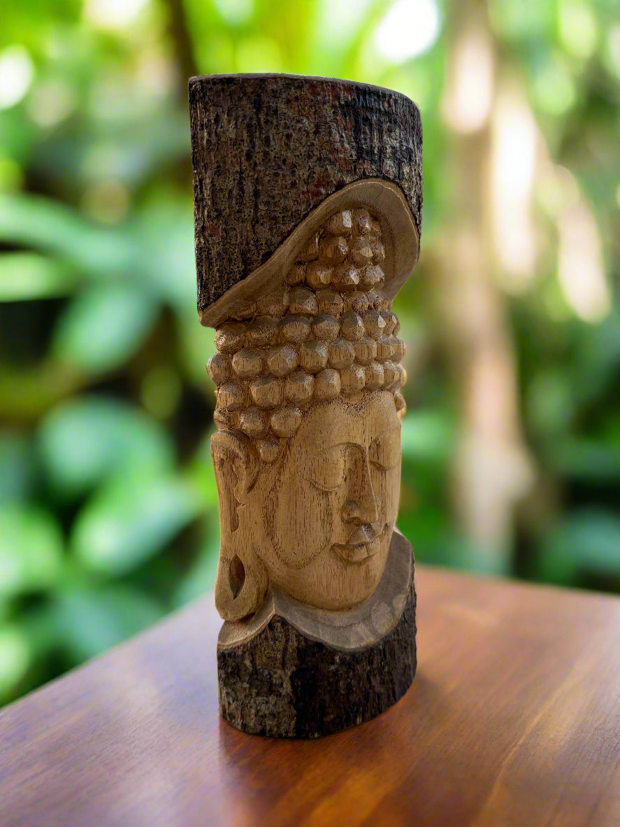 Wooden Buddha head carving on a tree log with a blurred green garden background