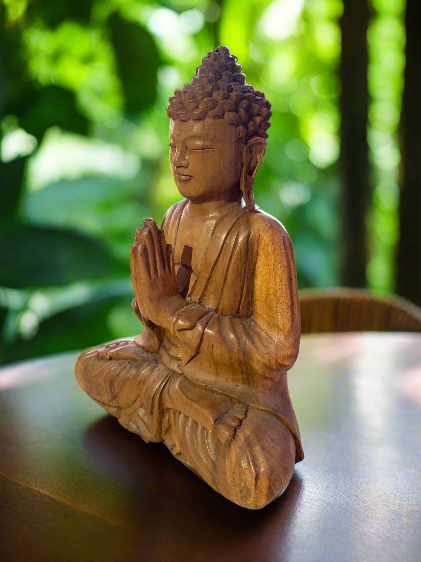Wooden Buddha statue in meditation pose on a table with a green garden background