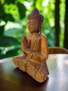 Wooden Buddha statue in meditation pose on a table with a green garden background